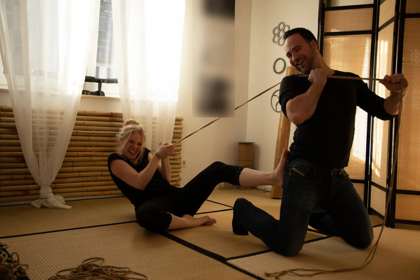 Lachendes Paar auf der Tatami: ein Seil verbindet beide, Leichtigkeit und Spaß im Shibari-Kurs